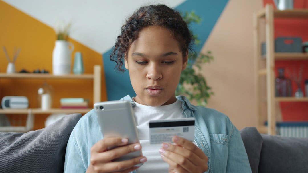 Young woman holding credit card and smartphone indoors