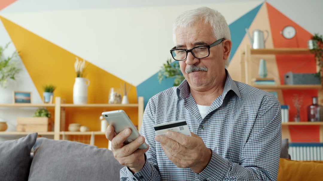 Elderly man using smartphone and credit card for online shopping.