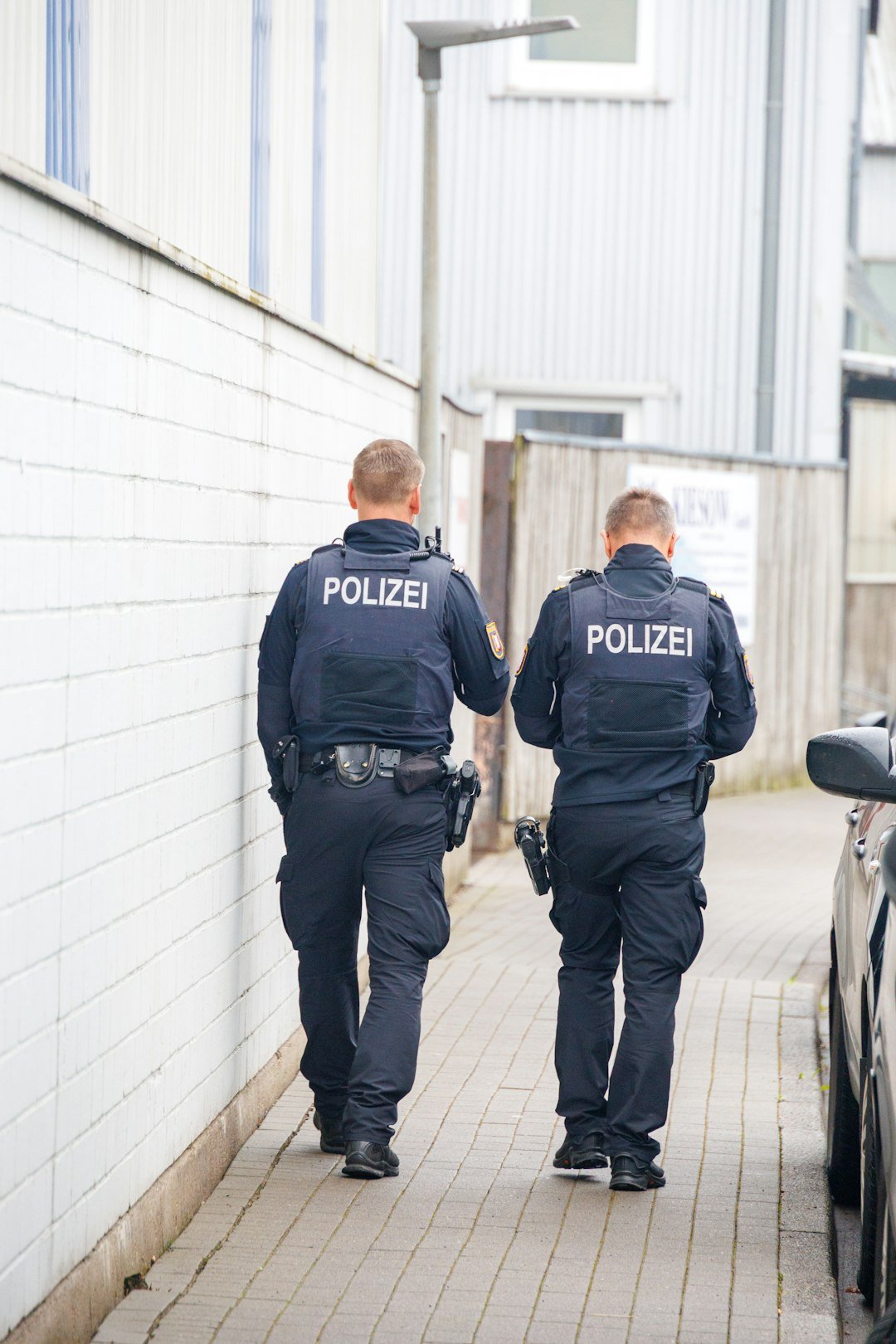 Two police officers walk down a narrow alleyway.